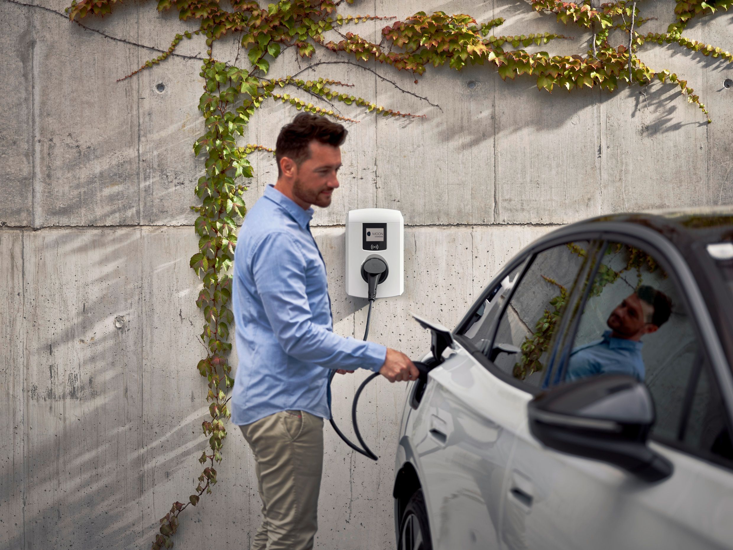 Mann lädt ein Auto mit einer Wallbox
