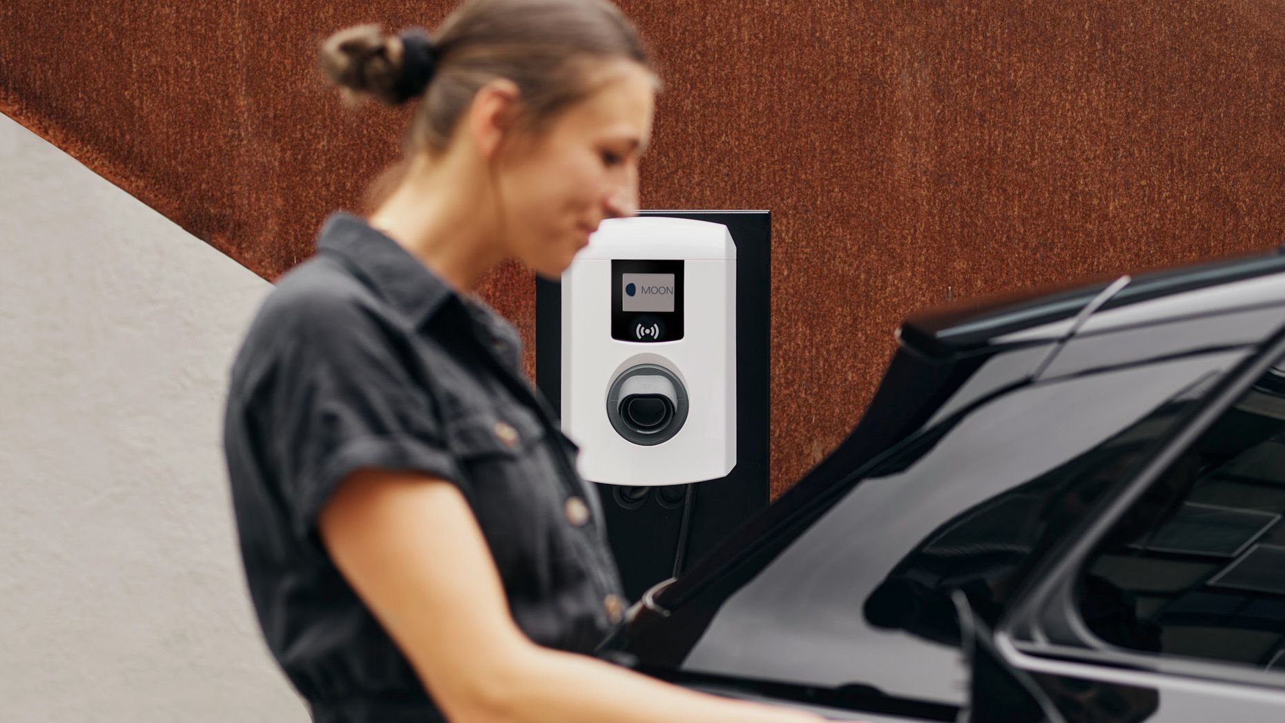 Frau steckt Zapfventil in ein E-Auto vor einer Wallbox