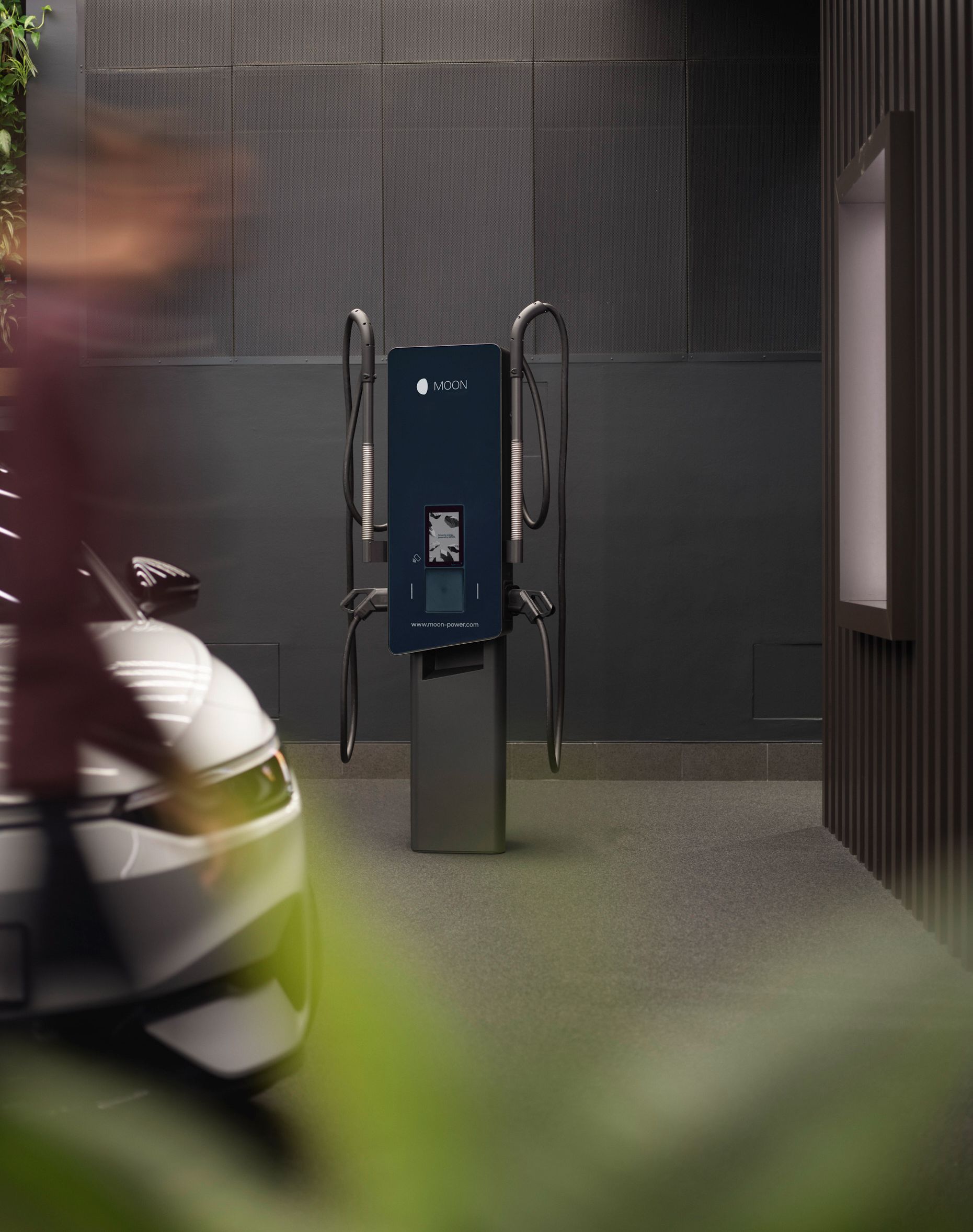 Wallbox vor einer grauen Wand mit E-Auto im Vordergrund