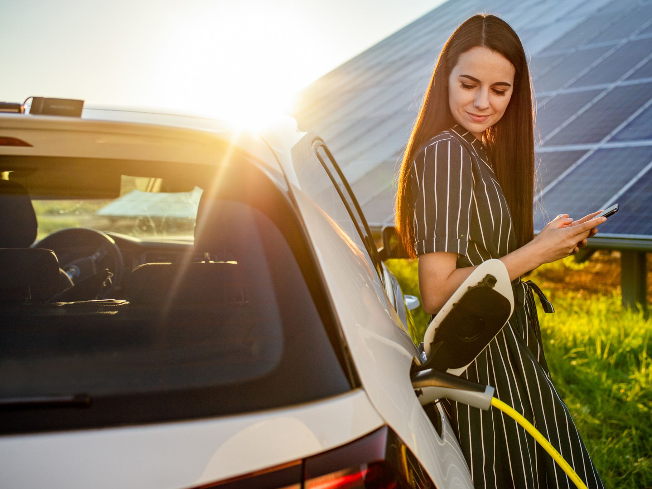 Frau lehnt an einem ladenden Auto vor einer Photovoltaikanlage