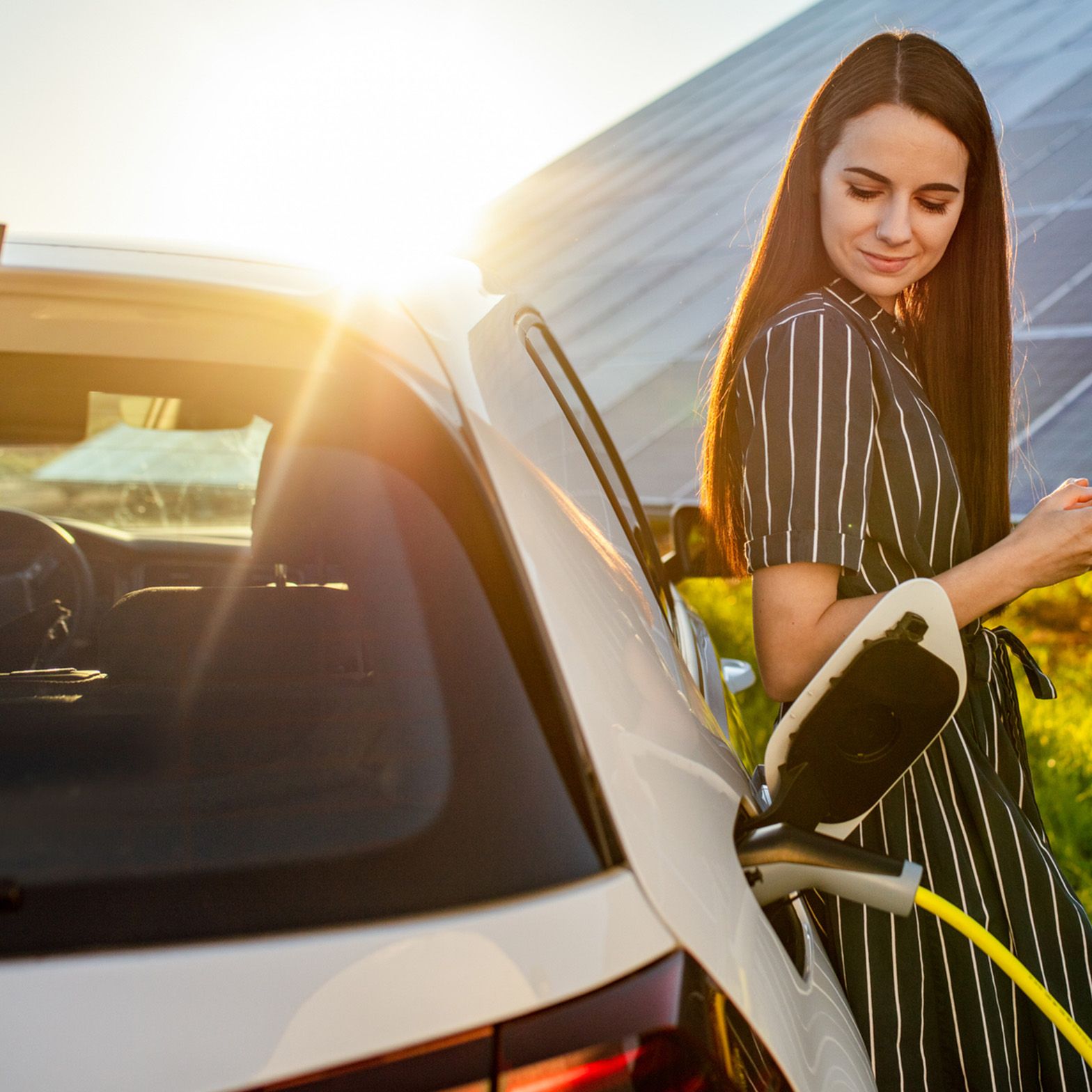 Frau lehnt an einem ladenden Auto vor einer Photovoltaikanlage