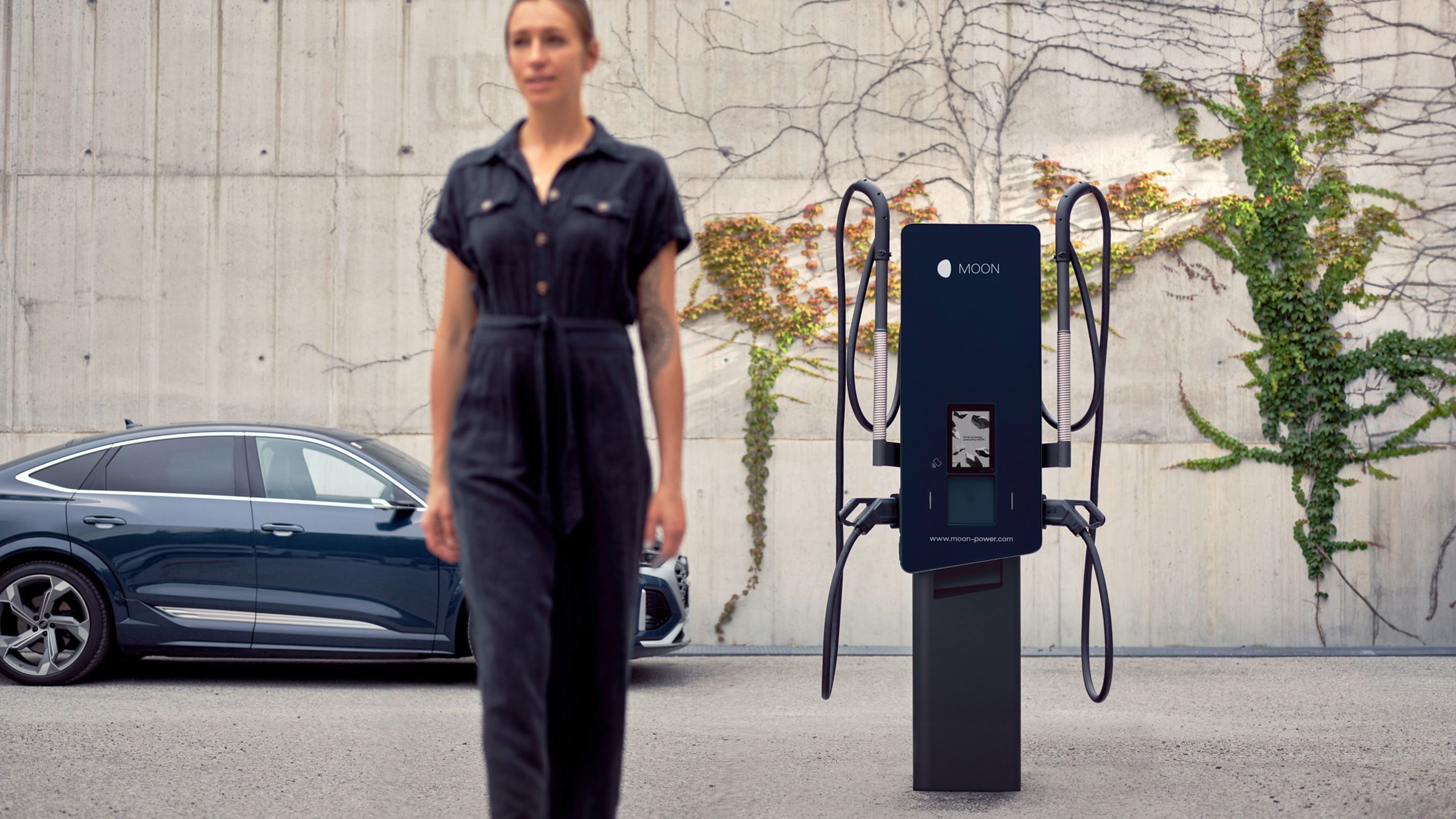 Frau geht vor einem E-Auto und einer Wallbox vorbei