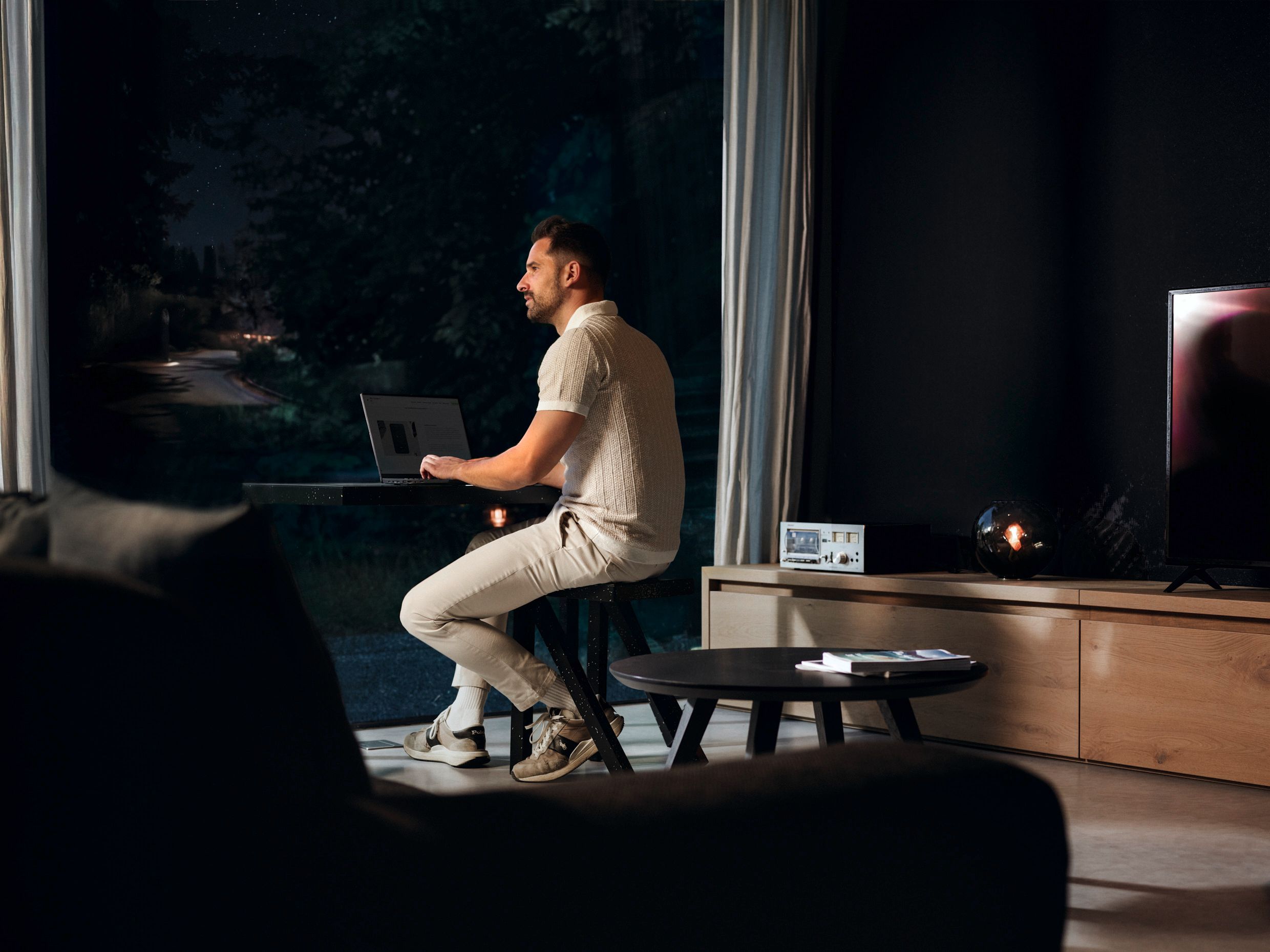 Mann arbeitet abends am Laptop im Wohnzimmer