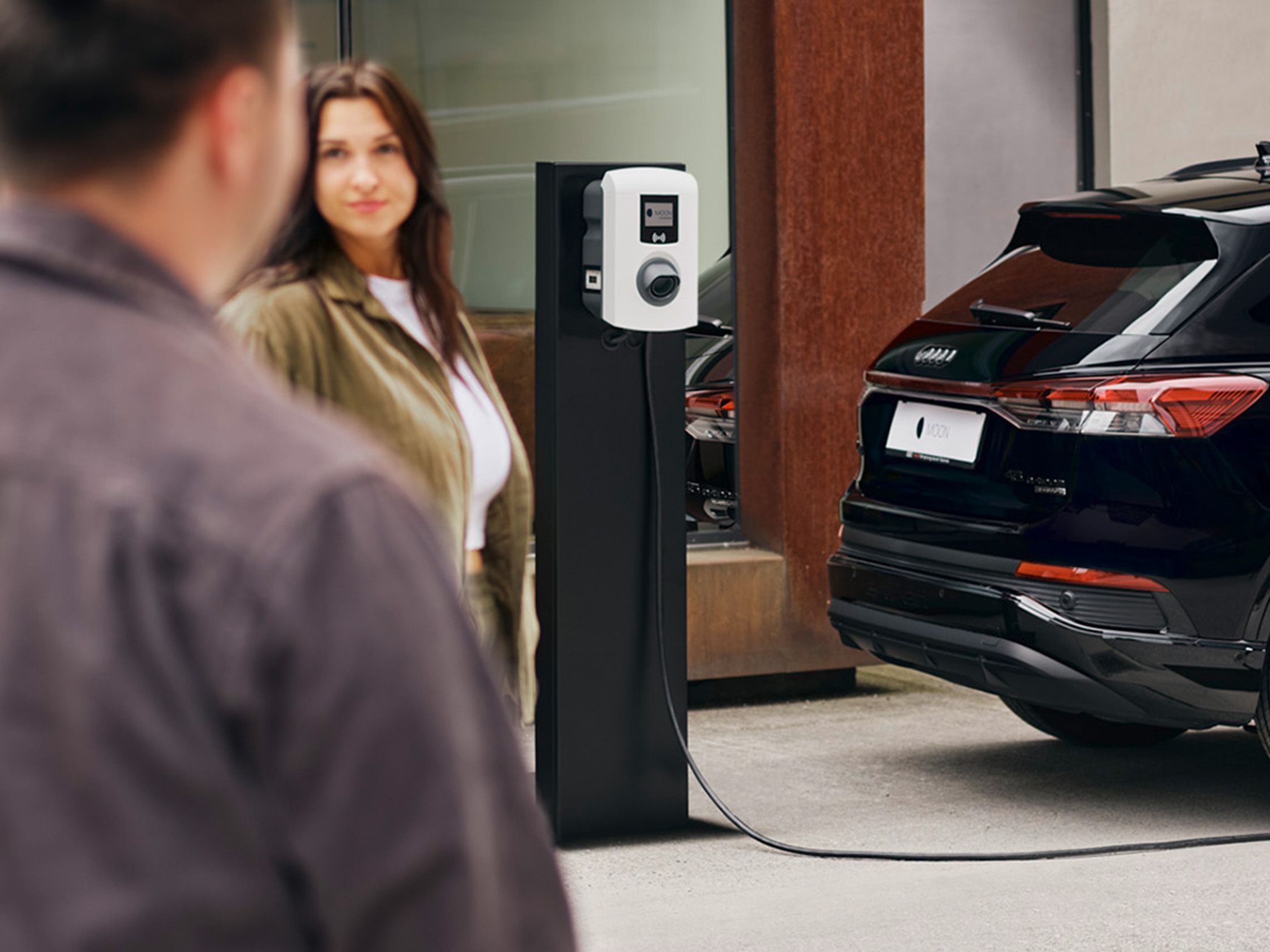 Ein Auto lädt an einer Ladestation mit zwei Menschen im Vordergrund