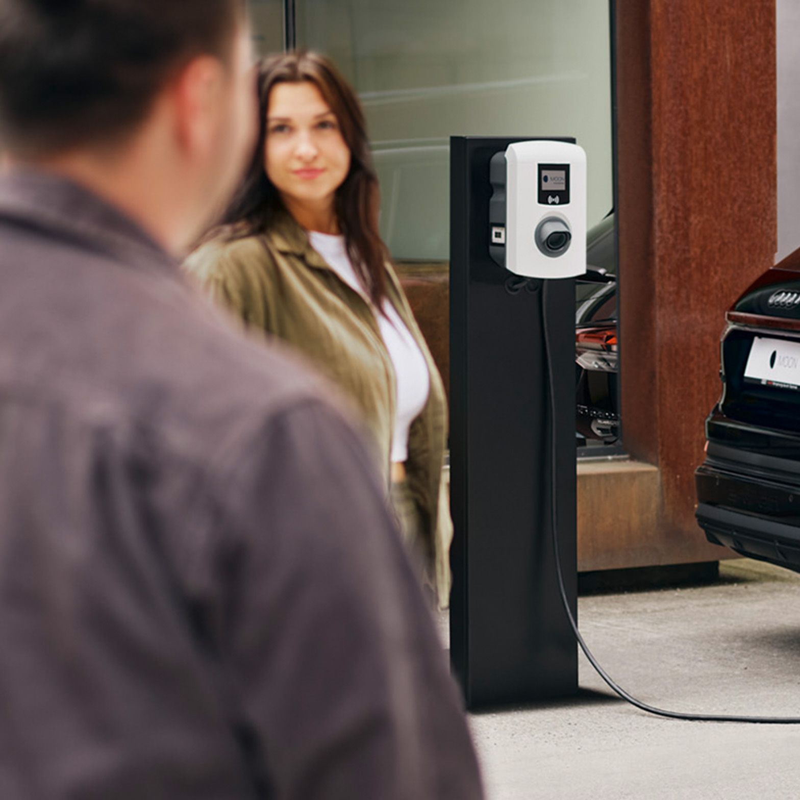 Ein Auto lädt an einer Ladestation mit zwei Menschen im Vordergrund