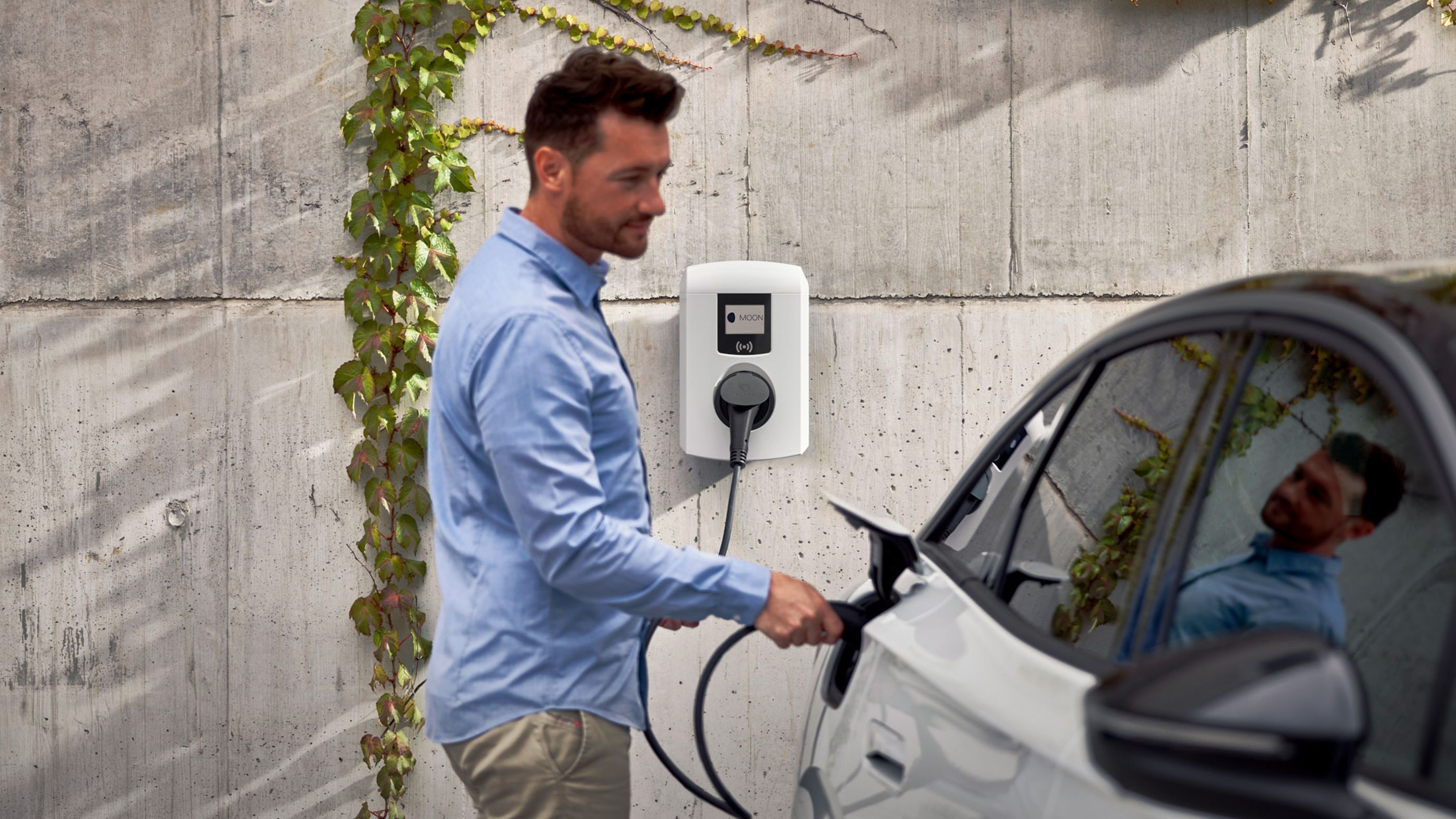 Mann steckt Zapfventil einer Wallbox in ein E-Auto