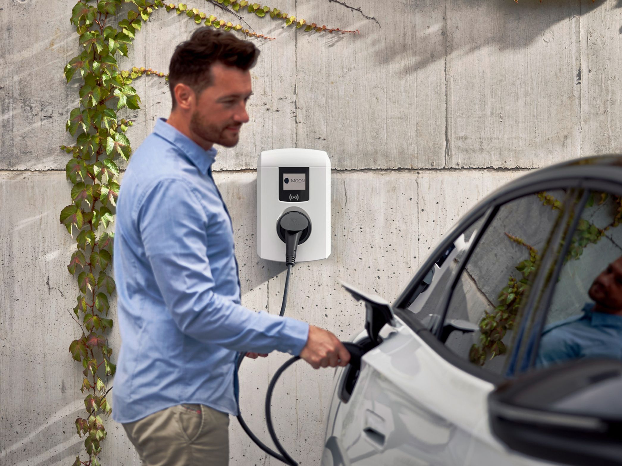 Mann steckt Zapfventil einer Wallbox in ein E-Auto