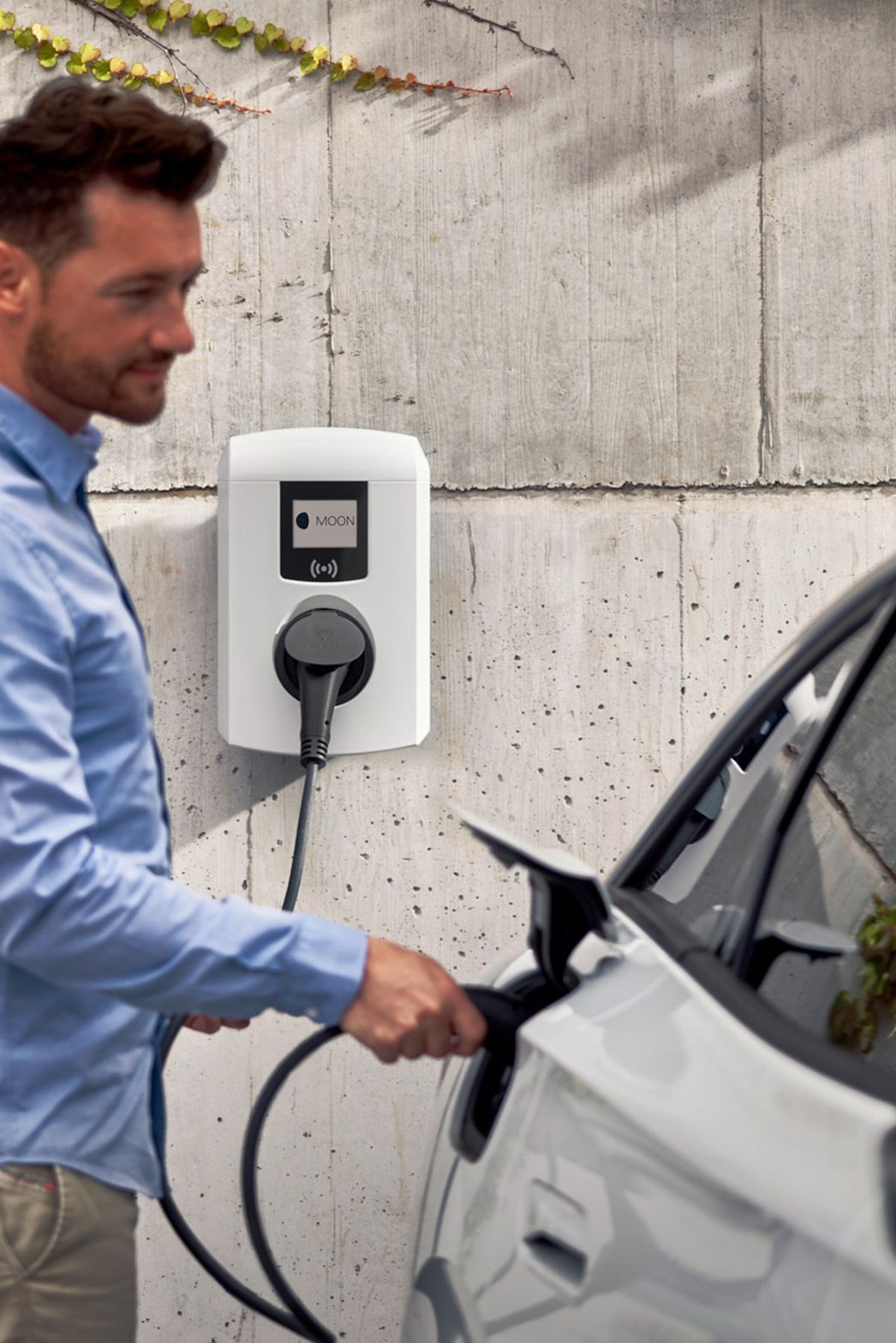 Mann steckt Zapfventil einer Wallbox in ein E-Auto