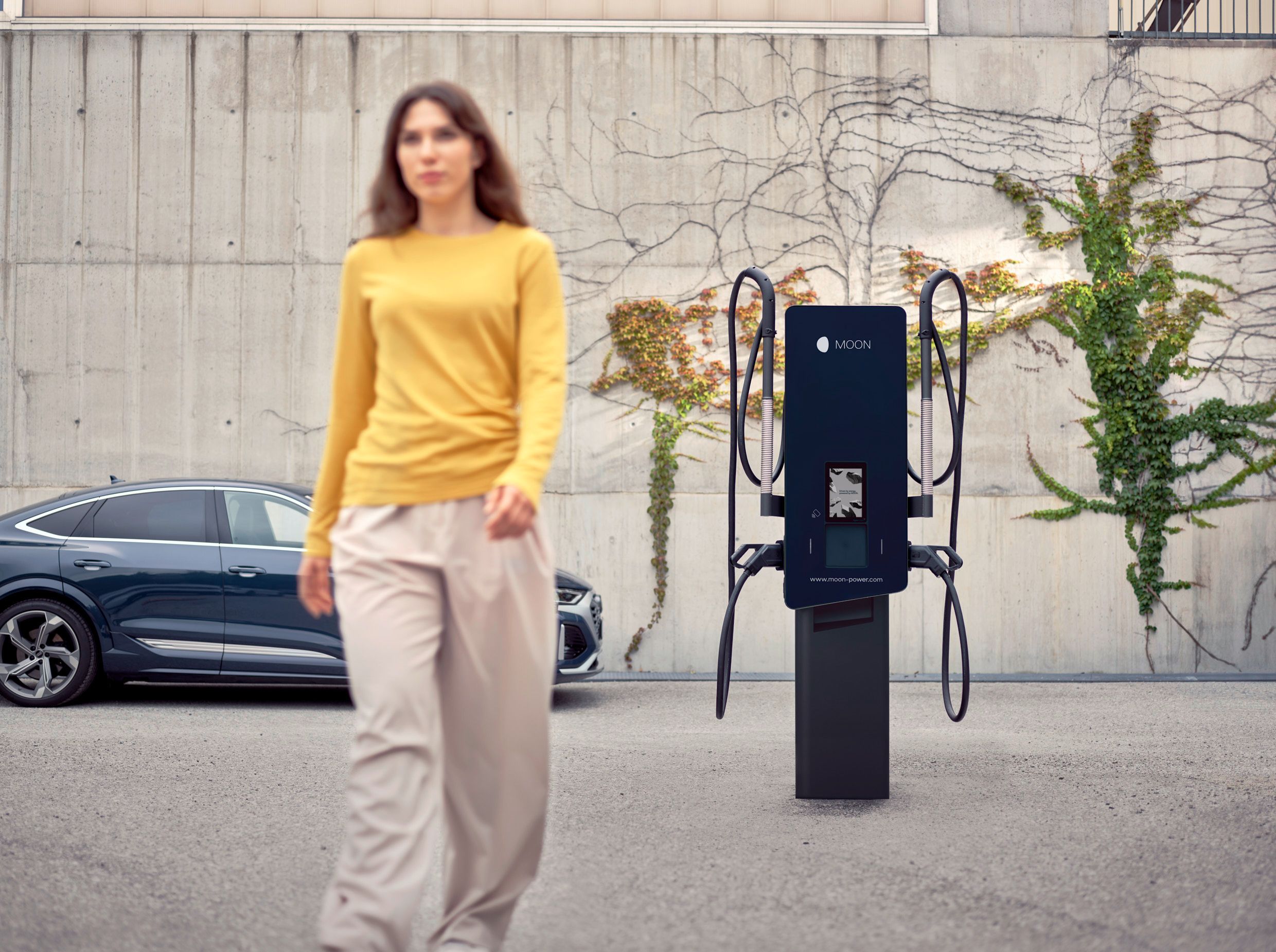 Frau geht von einer Wallbox vor einem E-Auto weg