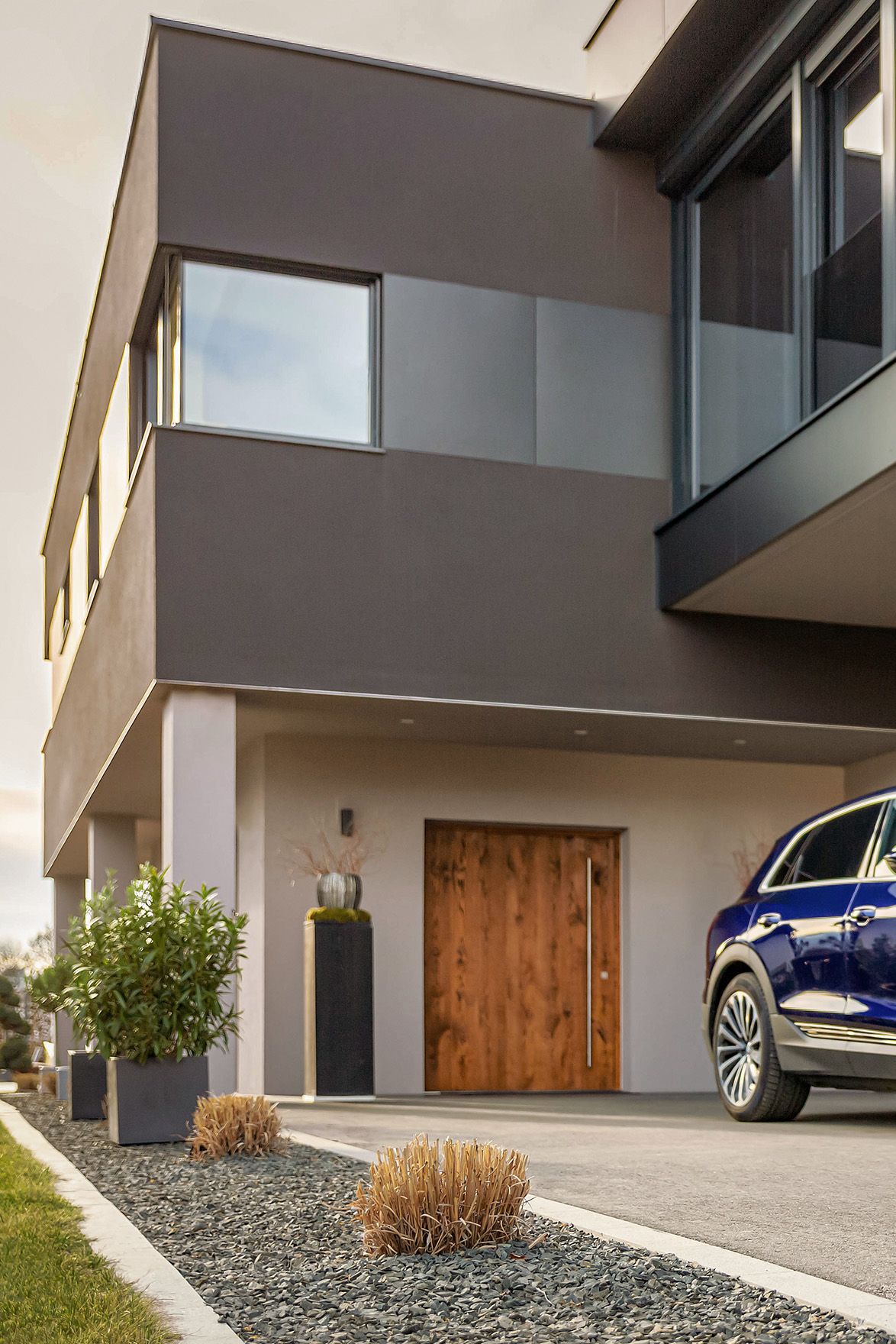 Mann geht mit einem Kabel in der Hand auf ein Auto bei einem Haus zu