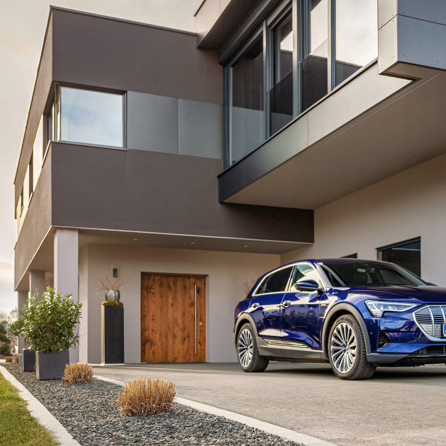 Mann geht mit einem POWER2Go Kabel in der Hand auf ein E-Auto bei einem Haus zu