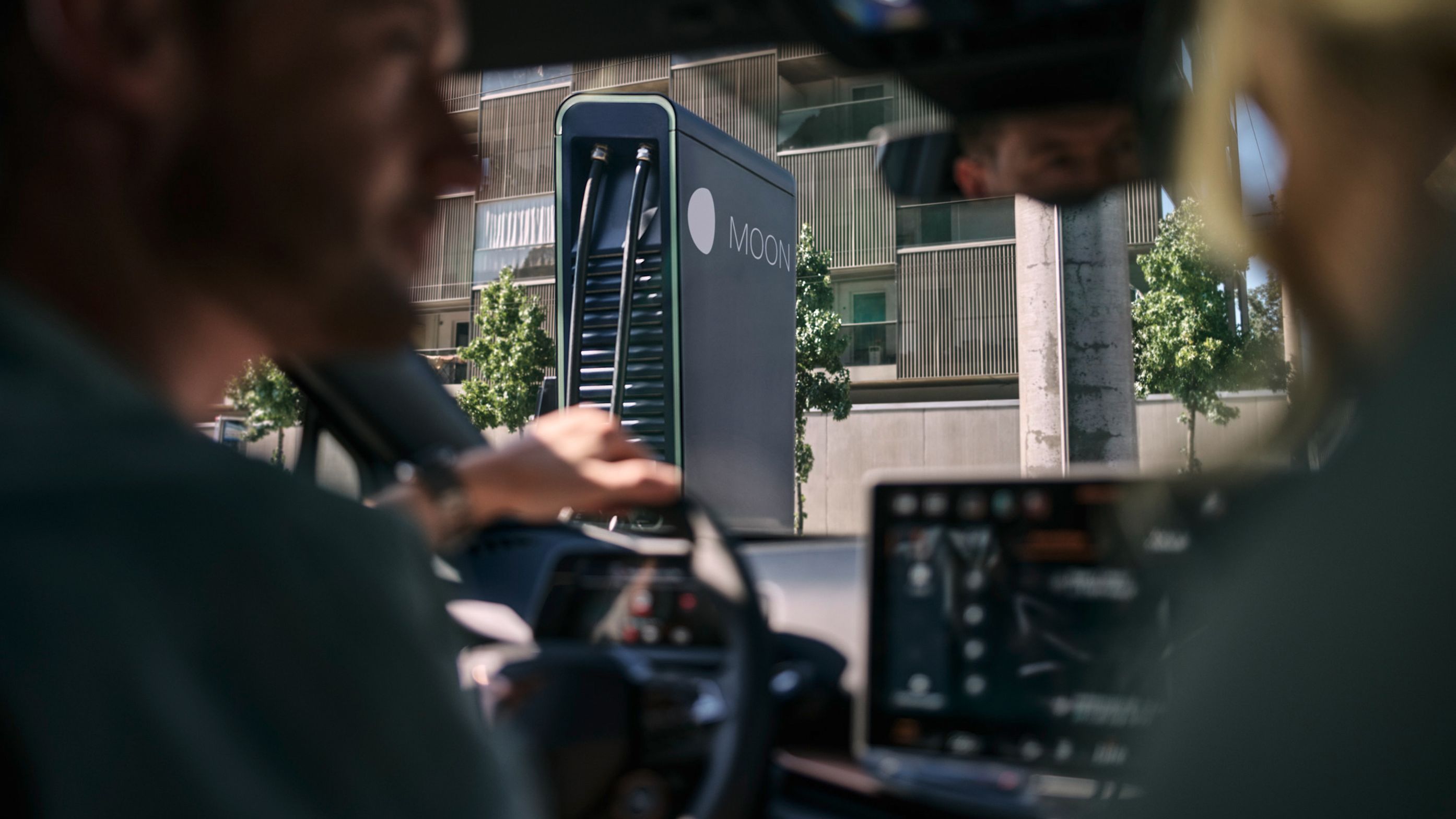 zwei Personen in einem E-Auto vor einer Schnellladestation