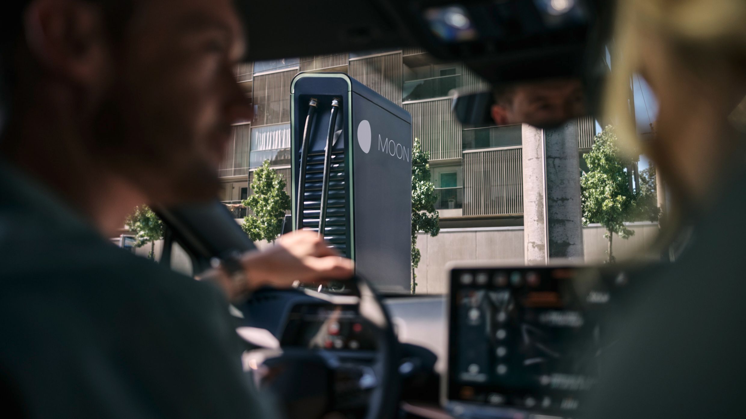 zwei Personen in einem E-Auto vor einer Schnellladestation