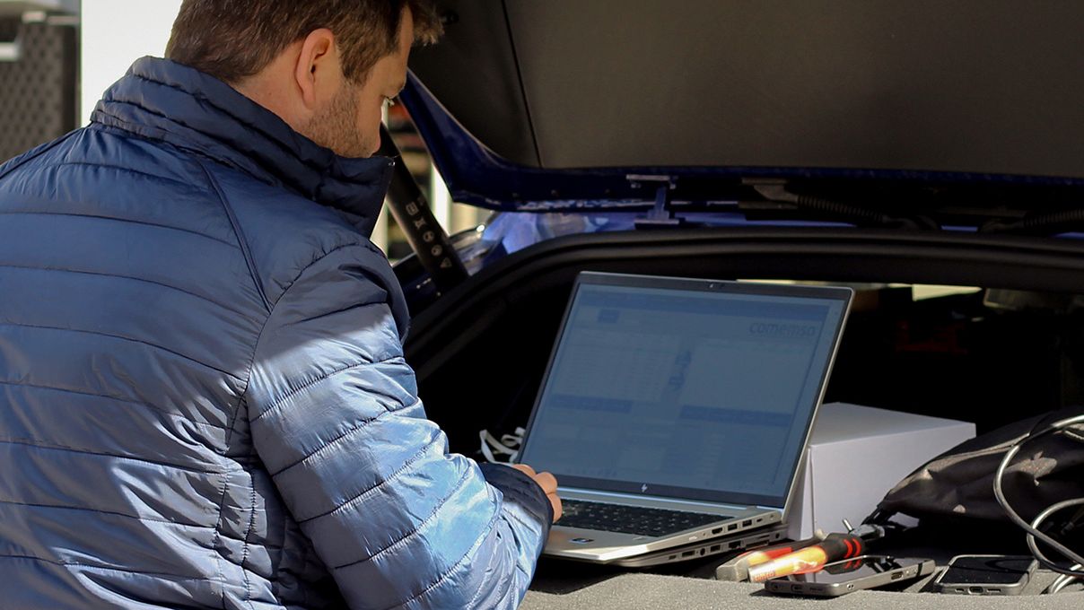 Mann mit Laptop der auf der Abdeckung eines Kofferraums steht
