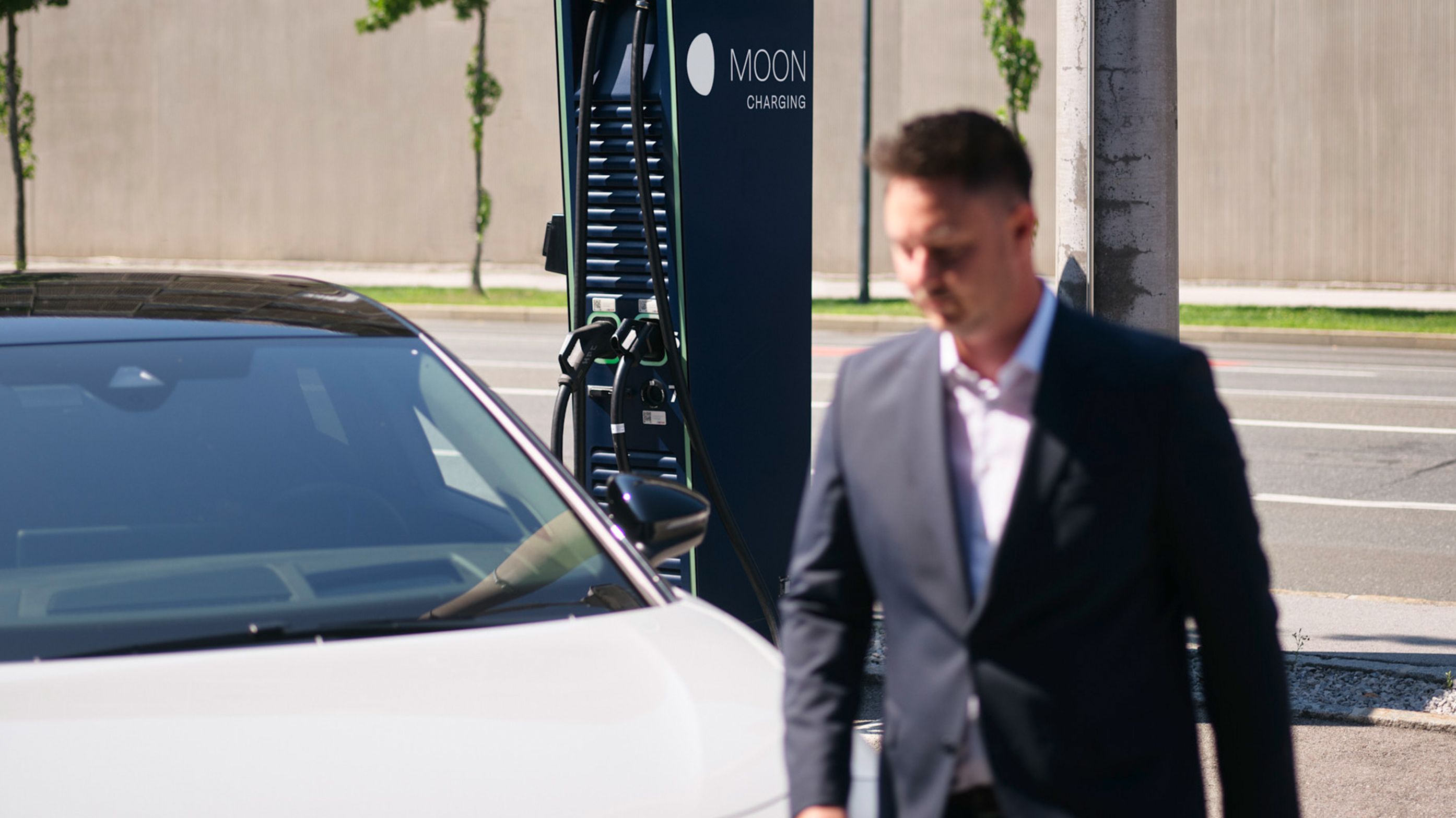 Mann geht vor einem Auto vor einer Ladestation vorbei