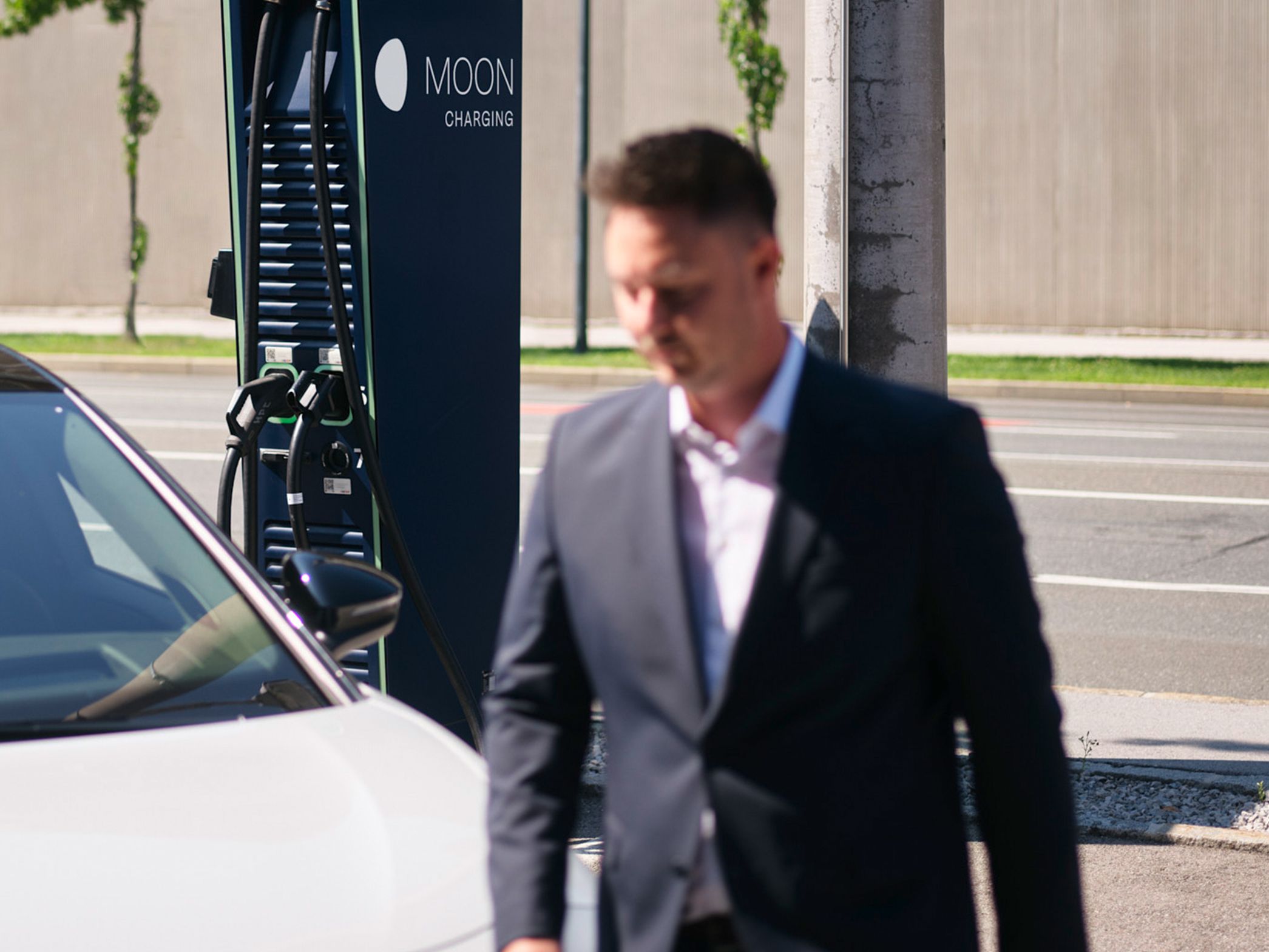 Mann geht vor einem Auto vor einer Ladestation vorbei