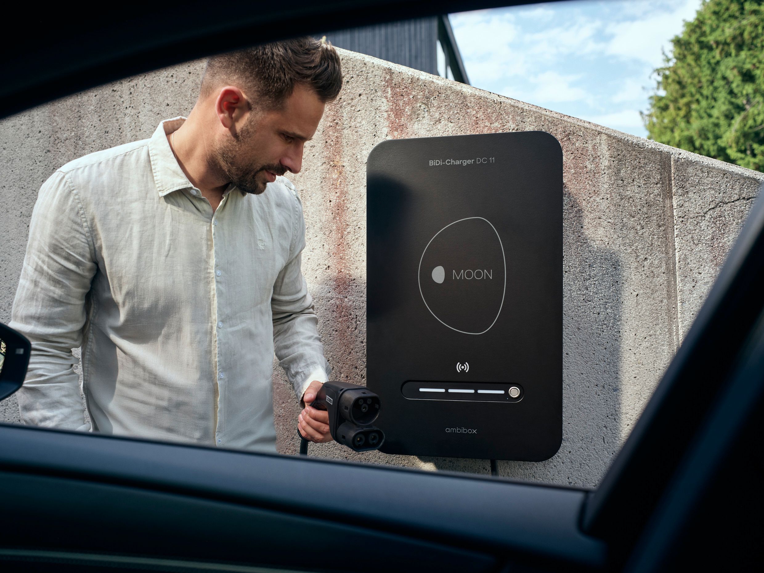 Mann vor BiDi Wallbox mit Stecker in der Hand