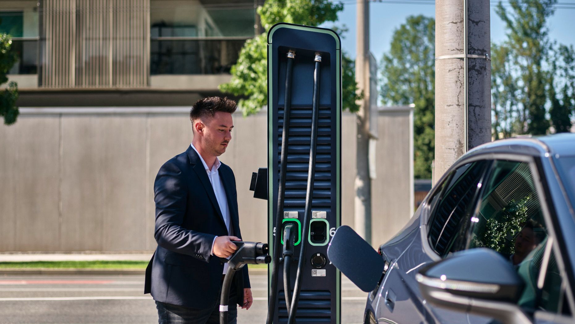 Mann hält Zapfventil einer Schnellladestation in der Hand und geht auf ein E-Auto zu
