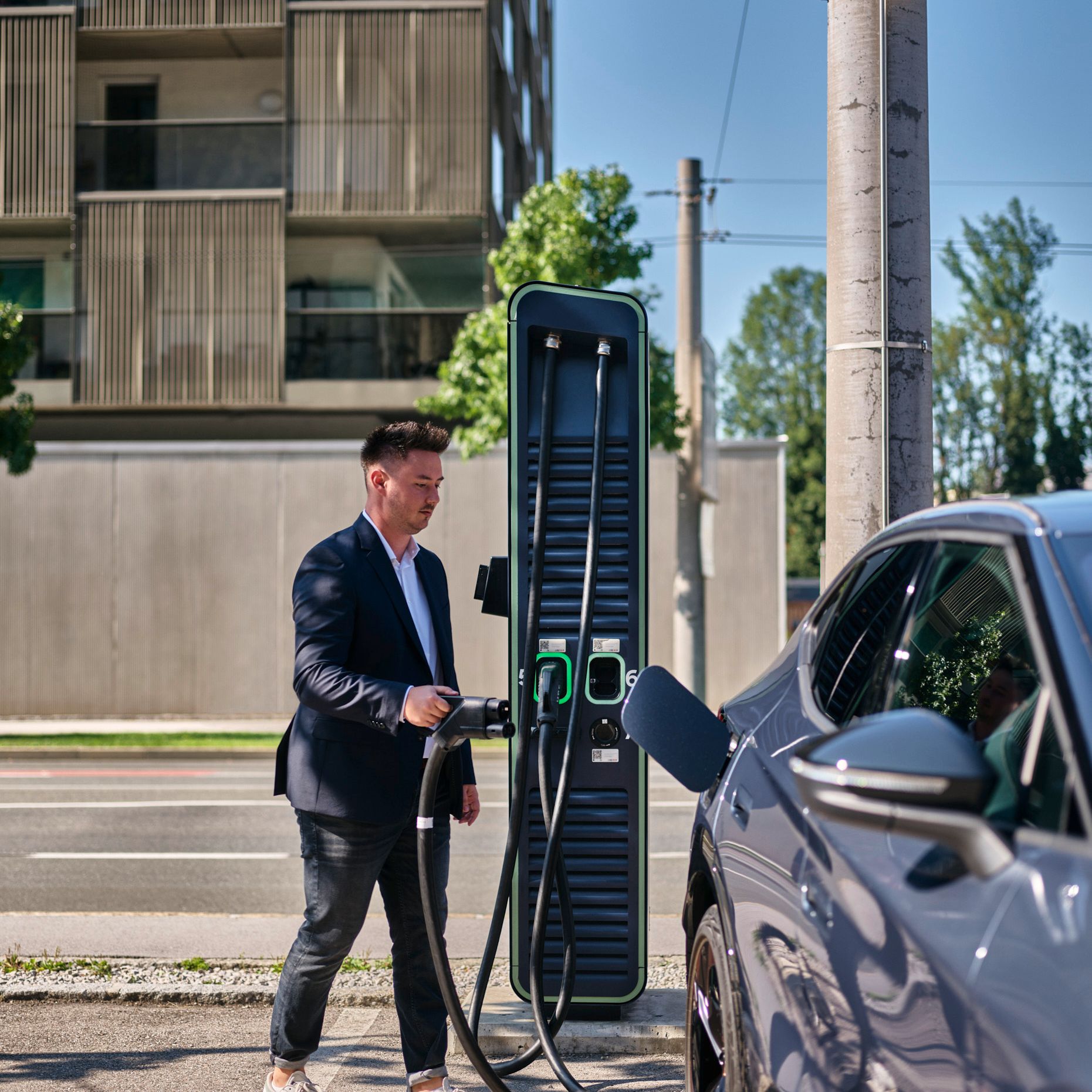 Mann hält Zapfventil einer Schnellladestation in der Hand und geht auf ein E-Auto zu