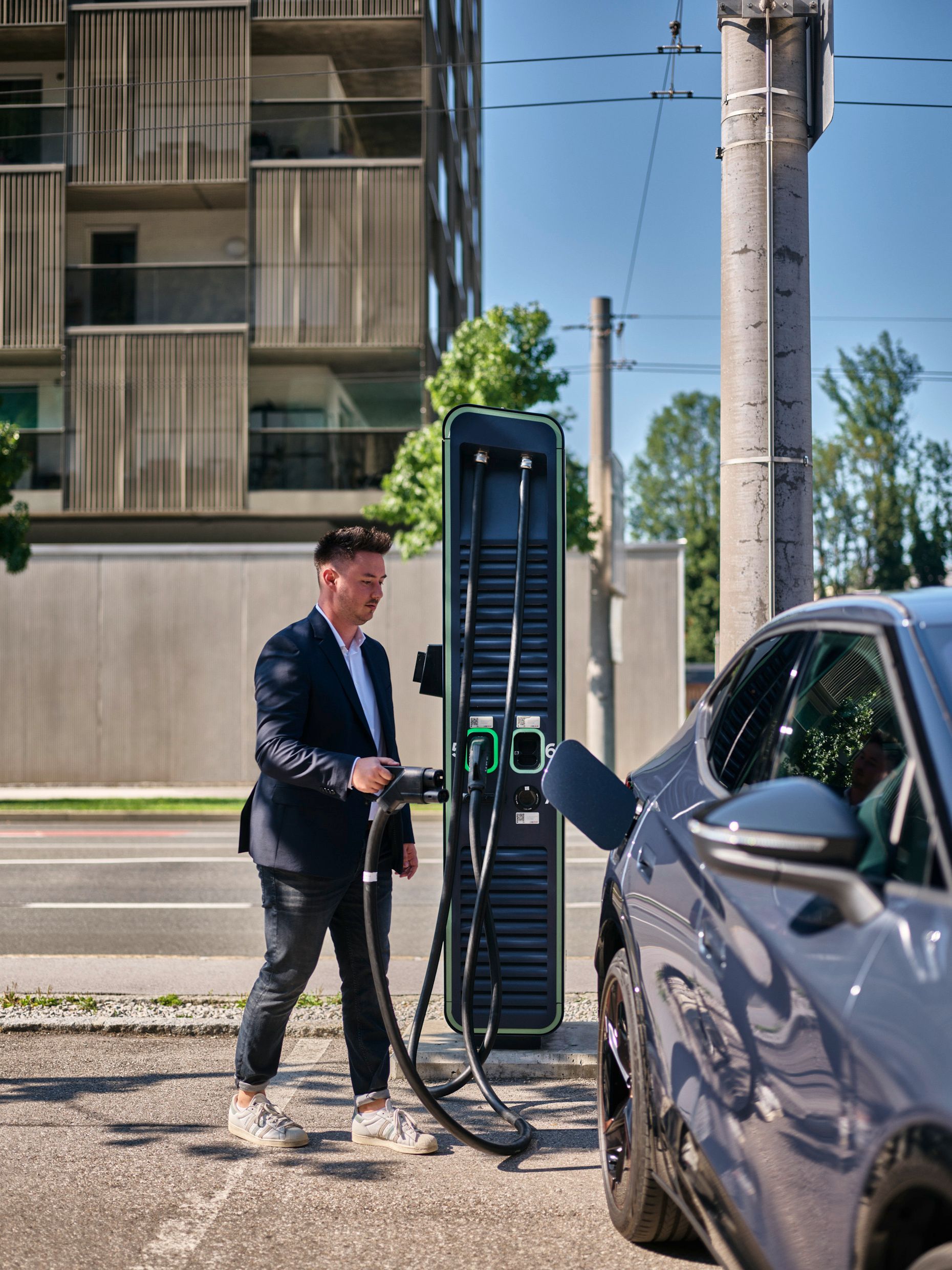 Mann hält Zapfventil einer Schnellladestation in der Hand und geht auf ein E-Auto zu